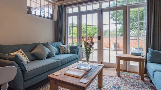 A cozy living room with a blue sofa, a wooden coffee table, and a patterned rug. - The Coach House Stables (Hernhill)
