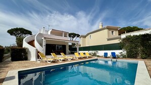A swimming pool with lounge chairs, a covered patio, and a two-story building with a tiled roof.