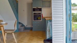 Una cocina con armarios azules, una mesa de comedor de madera con sillas, un radiador y una lámpara colgante.