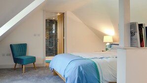Un dormitorio con una cama, una silla, una estantería y una puerta que da al baño.