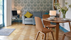 Una sala de estar moderna con un sofá gris, una mesa de comedor de madera y un televisor sobre un mueble.