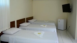A hotel room with three single beds, each with white linens and pillows, a small white refrigerator, and a mounted television on the wall.