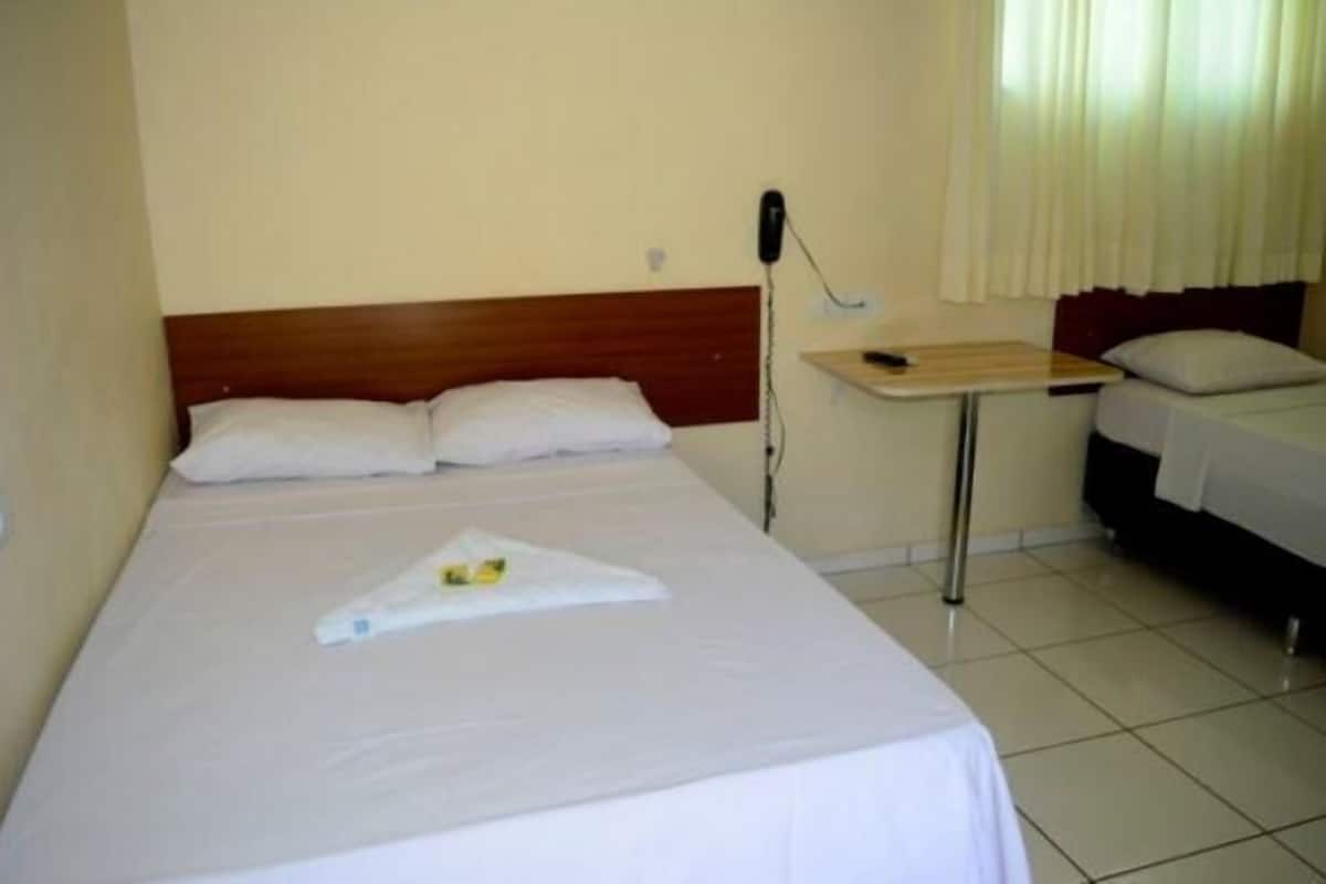A hotel room with a single bed, a bedside table with a phone, and a window with curtains.