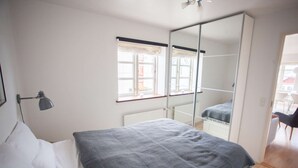 A bedroom with a bed, a bedside lamp, a window with curtains, a mirror, and a view of the outside.