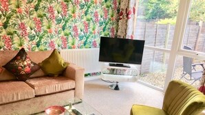 Una sala de estar con un sofá, una mesa de centro de vidrio, un televisor y un tapete estampado.