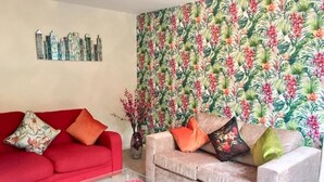 Una sala de estar con un sofá rojo, un sofá color beige y una mesa de centro de vidrio.