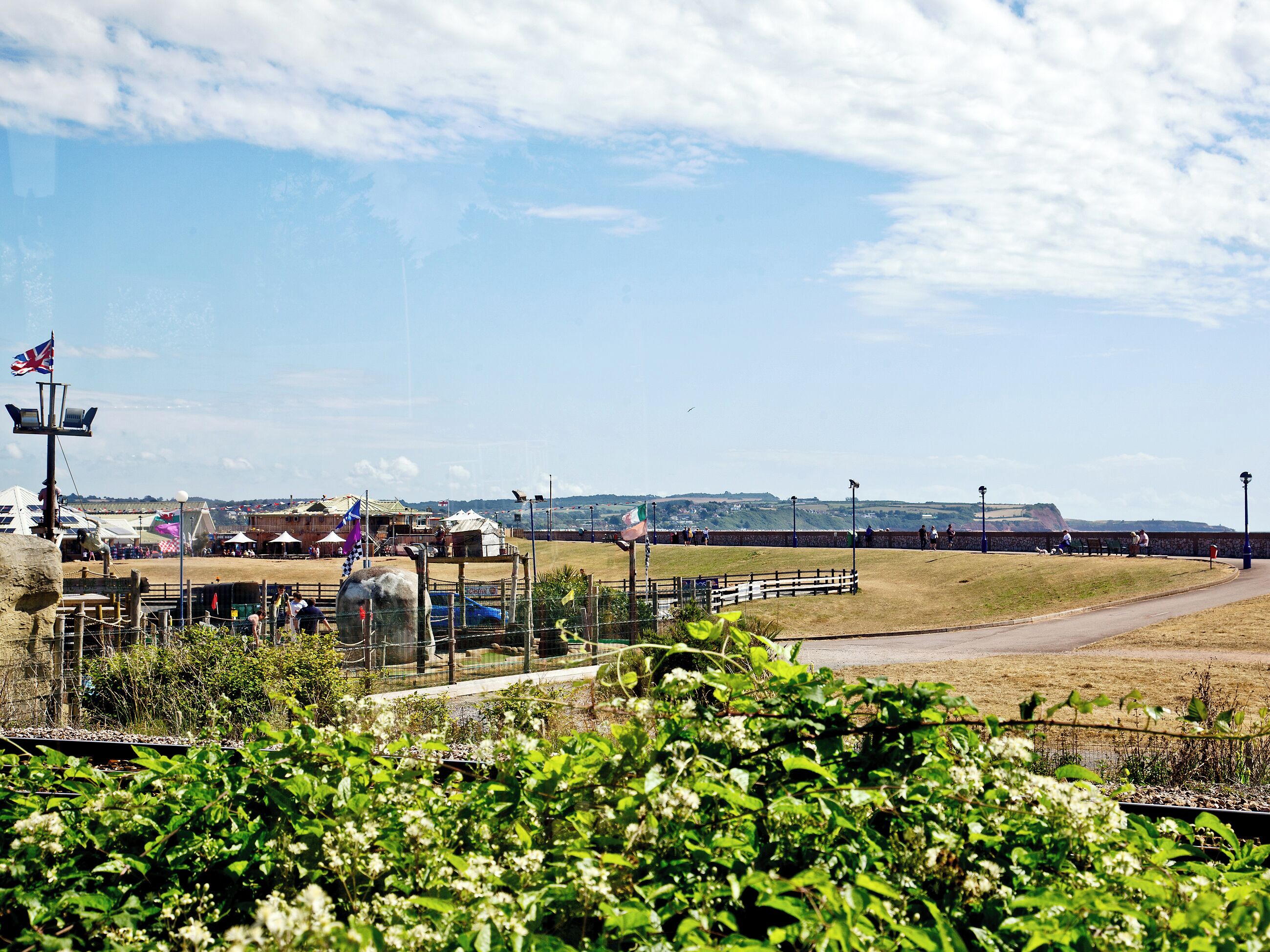 A coastal area with a fenced enclosure, a flag, and a distant view of hills.