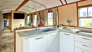 Eine kleine Küche mit Spüle, Arbeitsfläche und Schränken, einem Fenster mit Vorhängen und einem Spiegel über der Spüle.