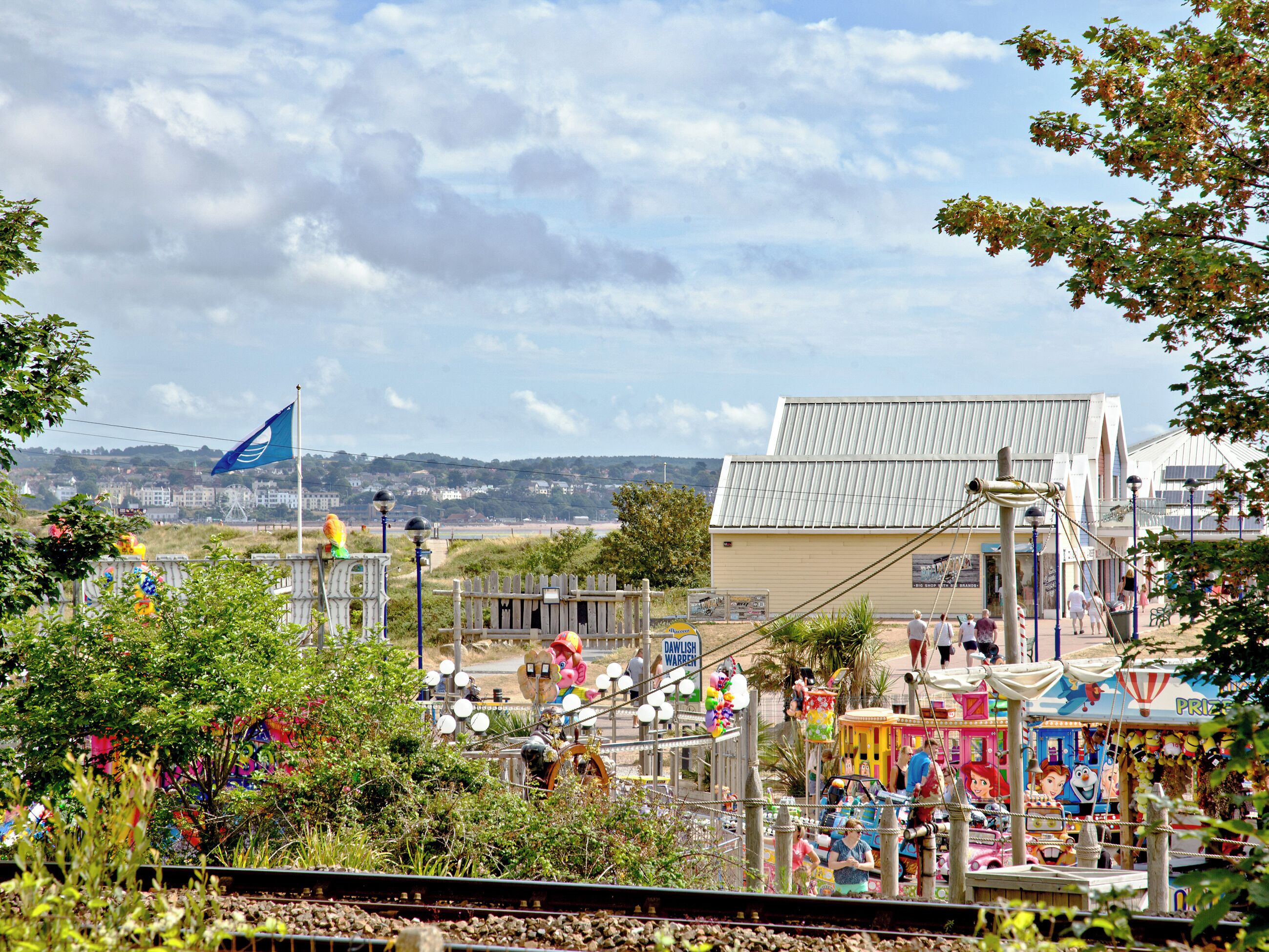 A seaside amusement park with a Ferris wheel, rides, and a large building in the background.