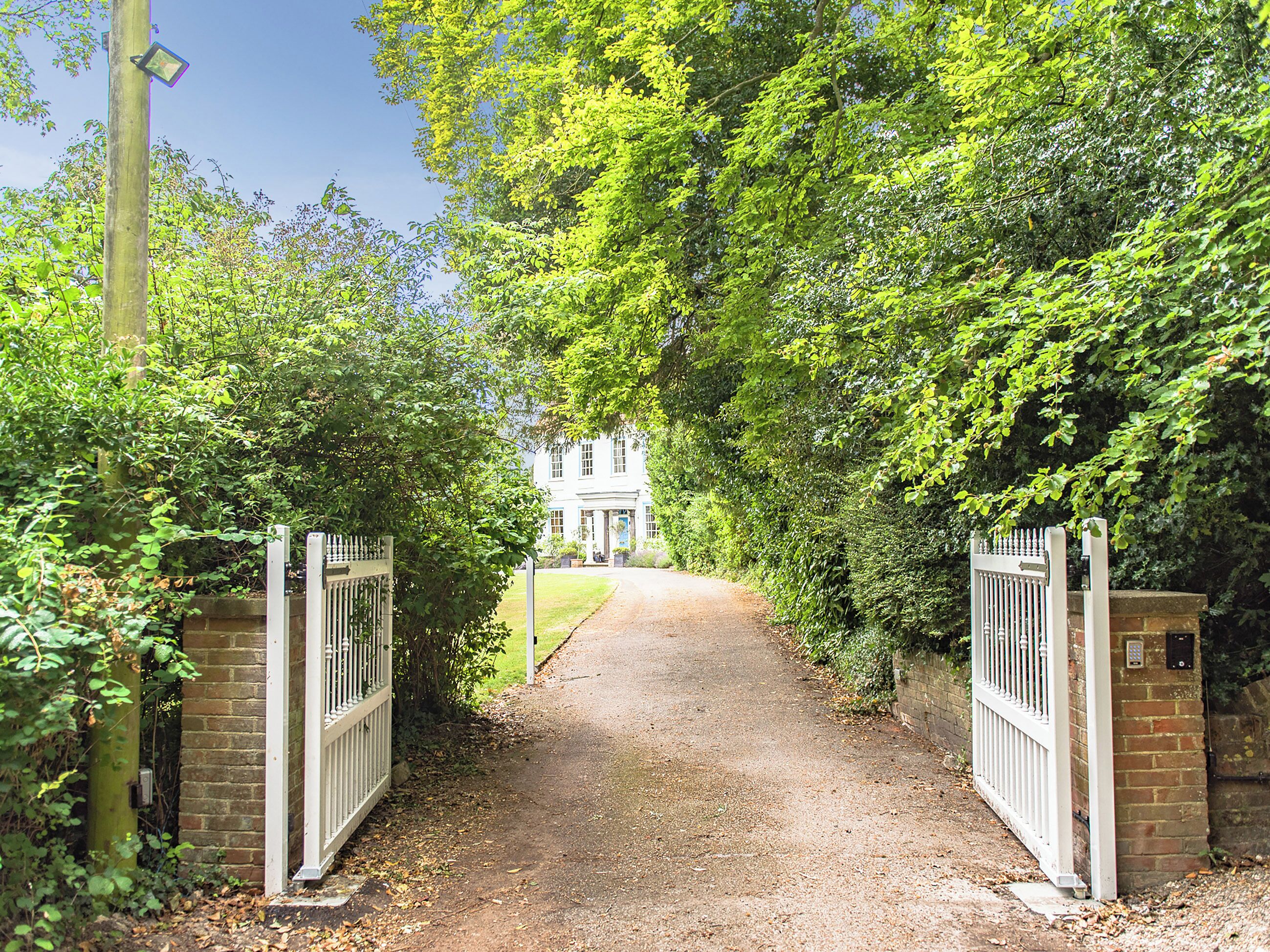 A gravel pathway leading to a white building with a blue door, surrounded by lush greenery.