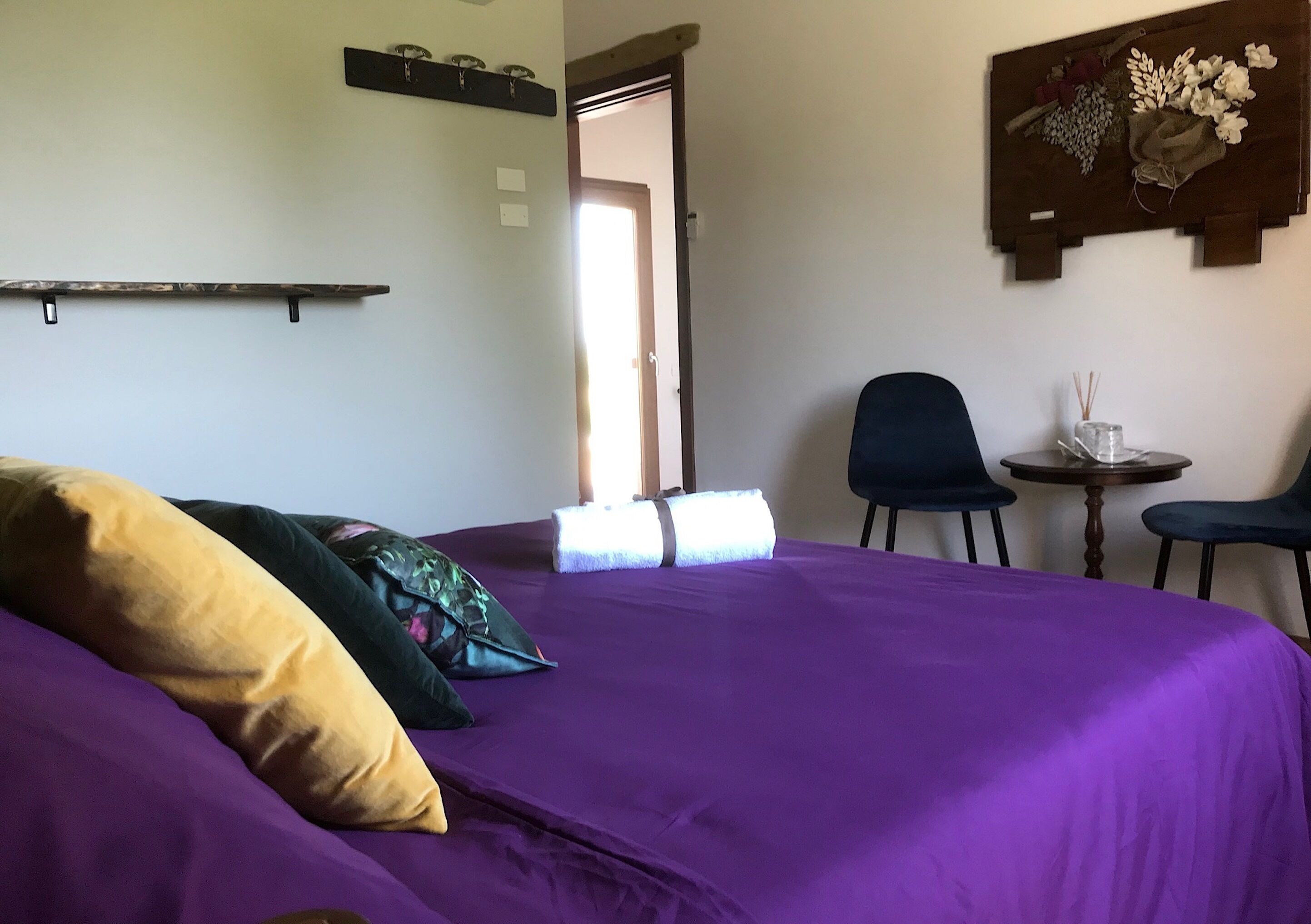 A room with a bed, two chairs, a small table, and a door leading to another room.