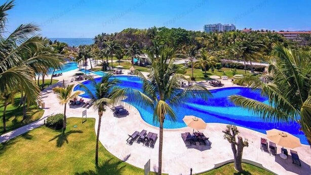 A resort with a large swimming pool surrounded by palm trees and lounge chairs. - Beautiful Beach front condo Villa Magna (Nuevo Vallarta)
