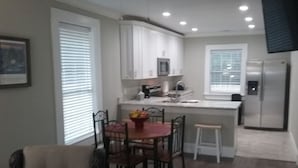 Una cocina moderna con armarios blancos, un refrigerador de acero inoxidable y un comedor con mesa y sillas.