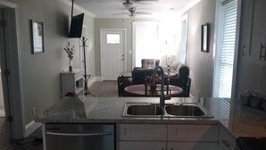 Una cocina con una isla central, doble lavaplatos y un comedor con sofá y mesa.