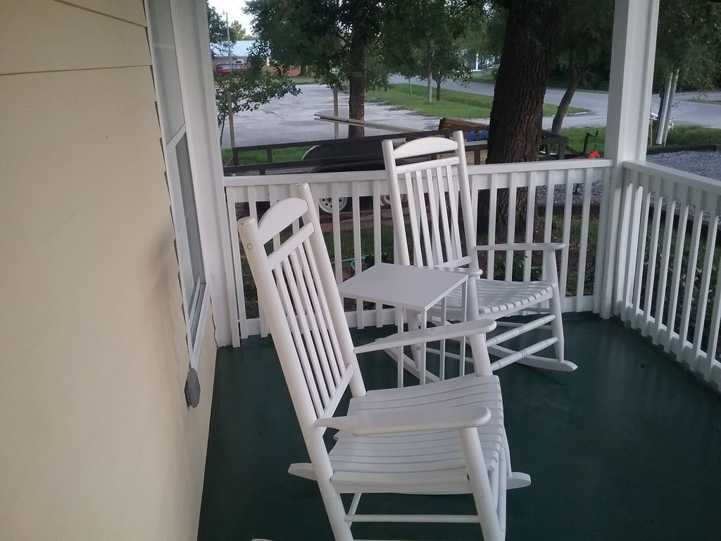 Une véranda avec des fauteuils à bascule blancs et une table.