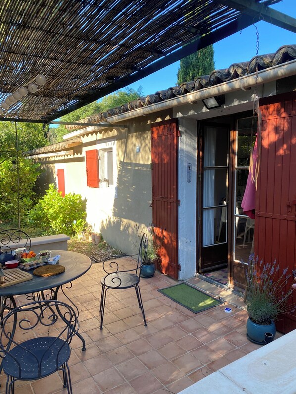 A patio with a table and chairs, a potted plant, and a building with a red door and windows.