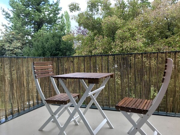 An outdoor seating area with a table and two chairs, surrounded by a bamboo fence and trees.
