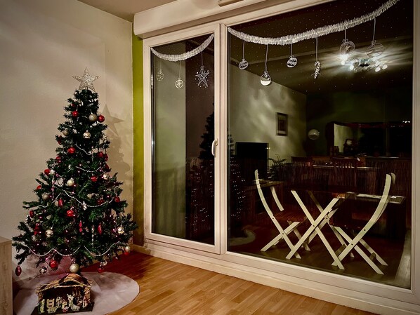 A Christmas tree with ornaments and lights, a nativity scene, and a dining area with chairs and a table.