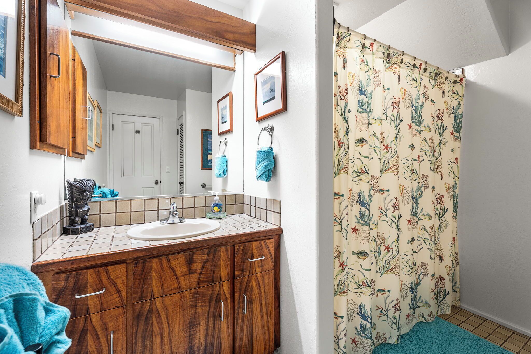Un baño con tocador de madera, lavabo, espejo y cortina de ducha con estampado floral.