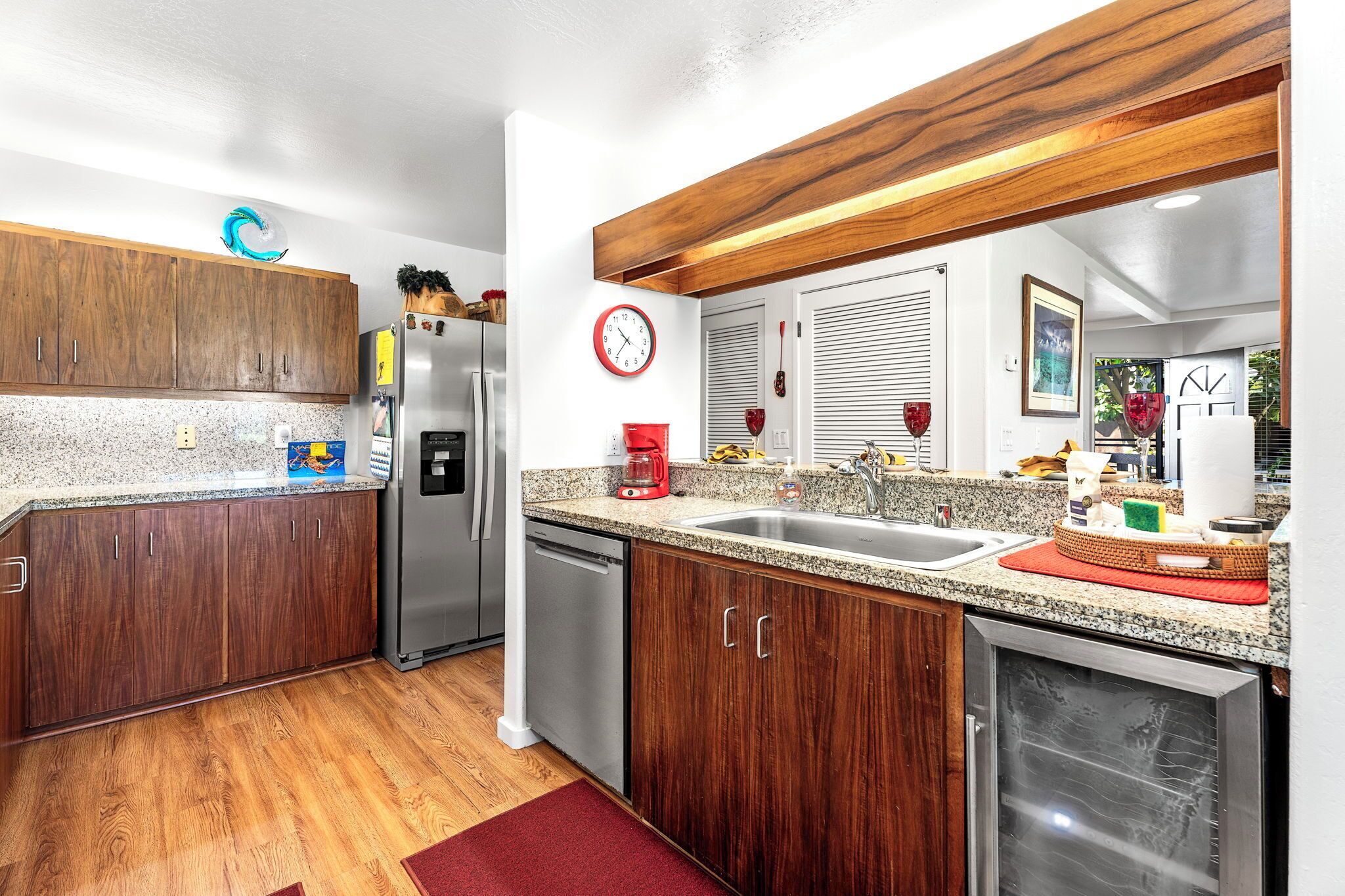 A modern kitchen with wooden cabinets, granite countertops, stainless steel appliances, and a red clock on the wall.