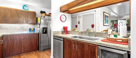 A modern kitchen with wooden cabinets, granite countertops, stainless steel appliances, and a red clock on the wall.