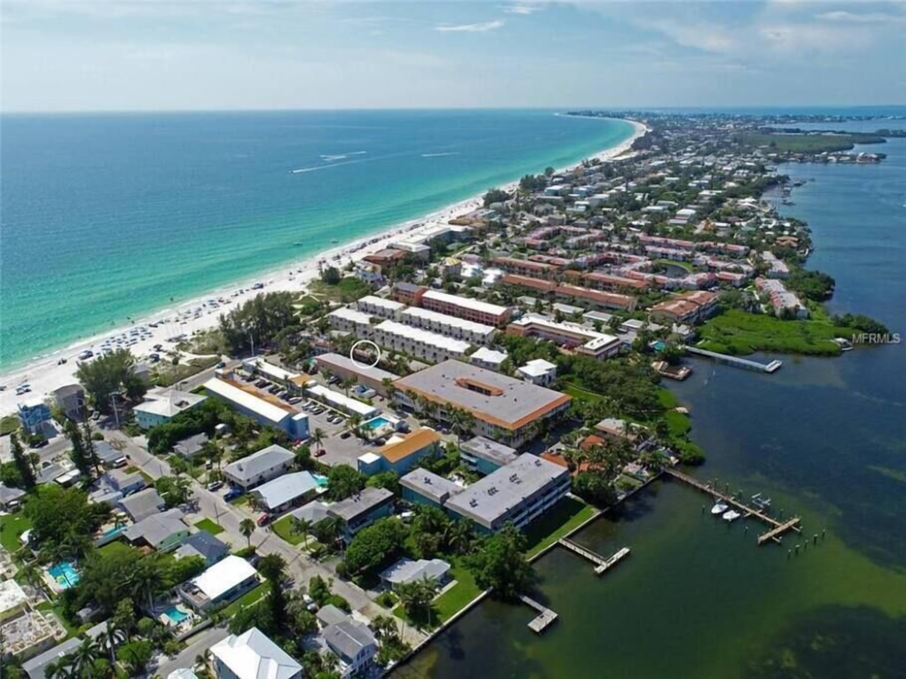 An aerial view of a coastal town with a beach, residential buildings, and a marina.