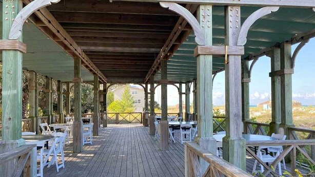 An outdoor wooden deck with tables and chairs, a covered area with a view of the landscape. - Tortuga Inn Beach Resort # 229 Island Condo, 2Bdrm (Bradenton Beach)