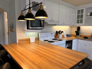 A kitchen with white cabinets, a wooden countertop, a microwave, a stove, and black pendant lights. - Tortuga Inn Beach Resort # 229 Island Condo, 2Bdrm (Bradenton Beach)
