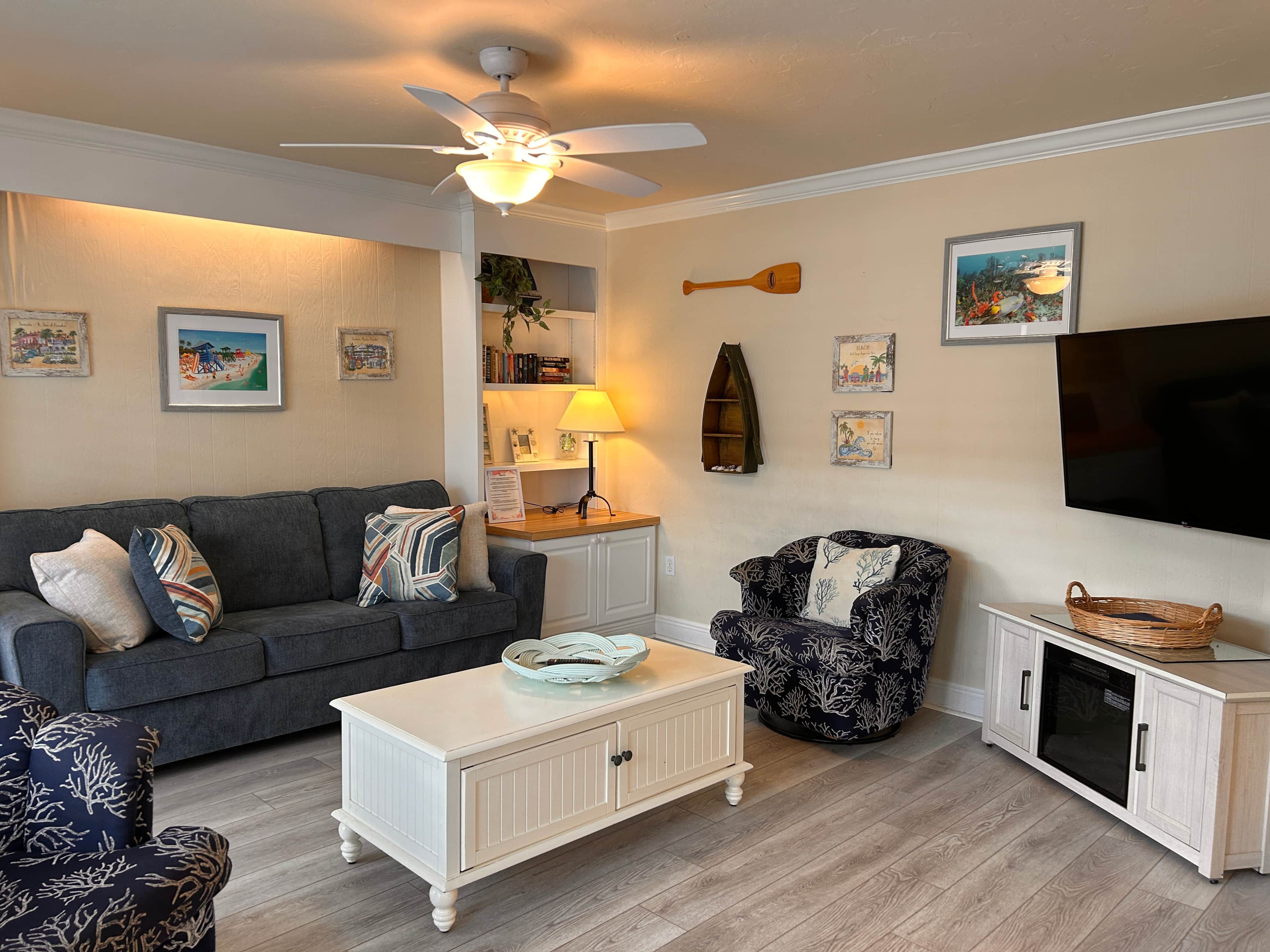 Ein Wohnzimmer mit Sofa, Sessel, Couchtisch, Fernseher und Deckenventilator.
