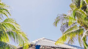 A beachside pavilion with blue pillars and a roof, surrounded by palm trees and beach chairs.
