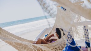 A hammock on a beach with a clear view of the ocean.