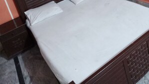 A neatly made bed with white linens in a room with a wooden headboard and a nightstand. - City Palace One (Lahore)