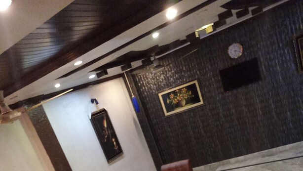 A room with a dark wall, a clock, a framed picture, and a seating area with a table and chairs. - City Palace One (Lahore)