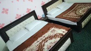 A hotel room with two beds, each with a headboard and a pillow. The walls have floral wallpaper, and there is a small shelf with framed pictures. - City Palace One (Lahore)