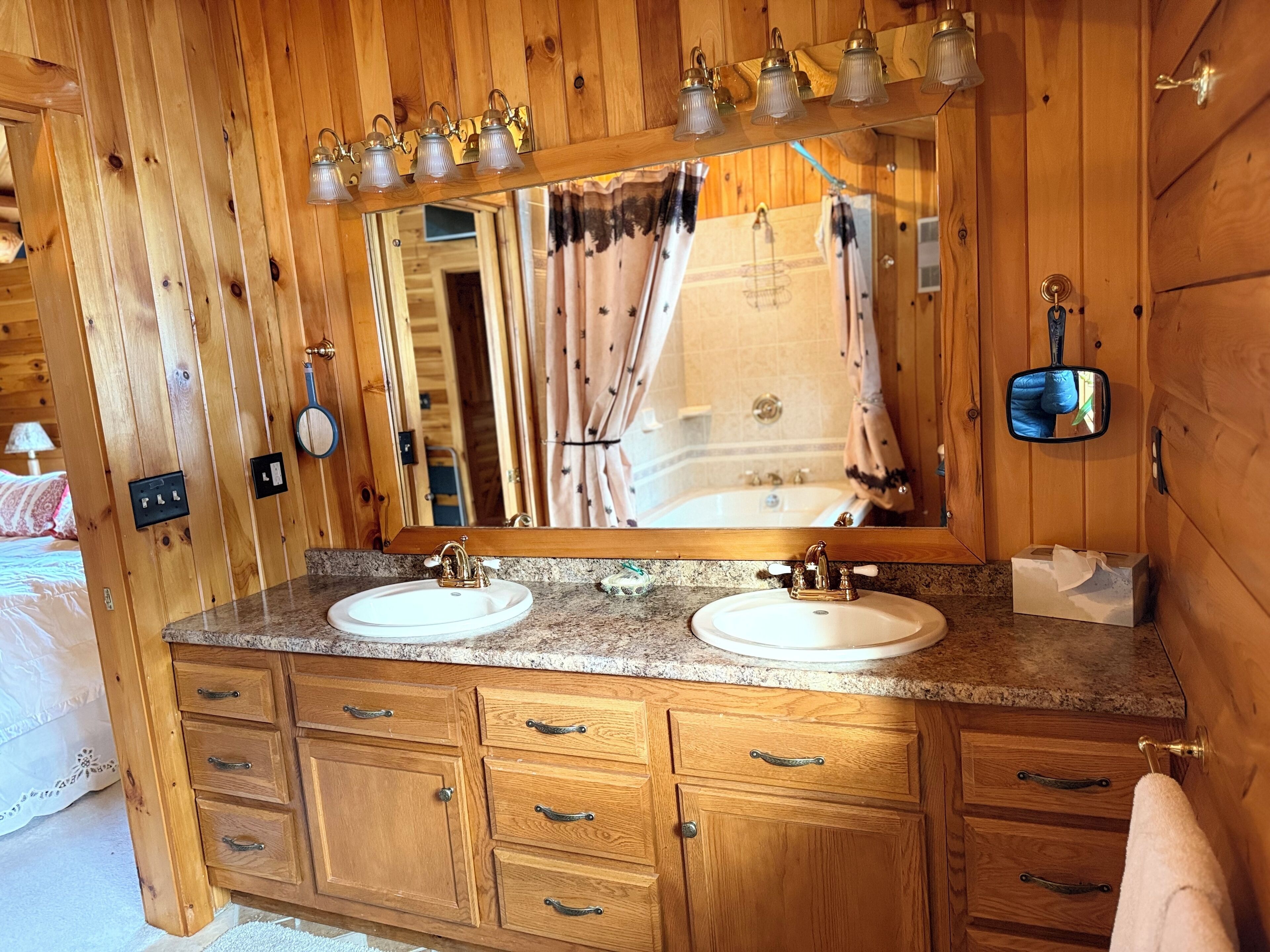 Een houten badkamer in een hutje, met twee wasbakken, een spiegel en een wastafelmeubel met lades.