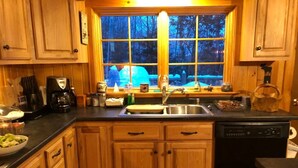 Une cuisine avec des meubles en bois, un évier, une machine à café et une fenêtre donnant sur des arbres.