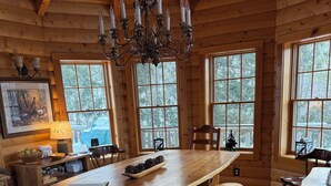 L’intérieur d’un chalet en bois, avec une grande table à manger, des bancs et un lustre.