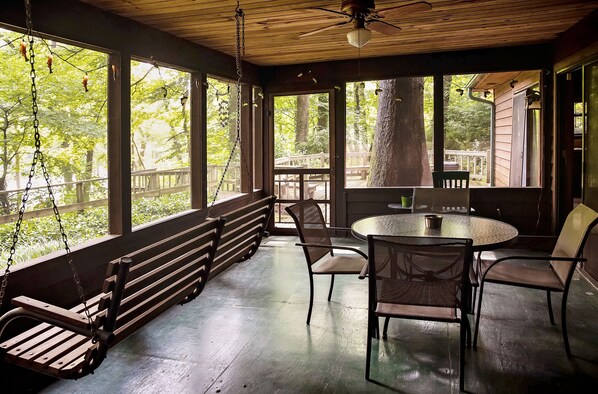 A covered porch with a swing, a round table, and chairs.
