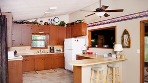 A kitchen with wooden cabinets, a white refrigerator, a window, and a ceiling fan.