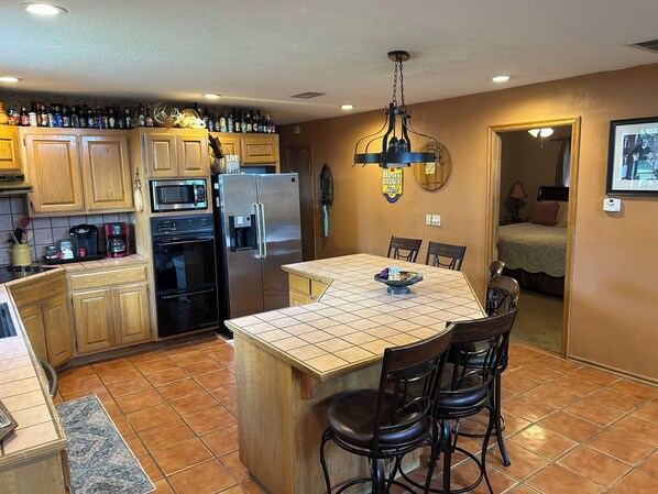 A kitchen with wooden cabinets, a stainless steel refrigerator, a microwave, and a coffee maker. There is a dining area with a table and chairs. - Skiatook Lake House Getaway (Sperry)
