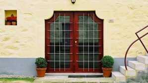 A building with a red door, two potted plants, and a small window with flowers. - Quinta do Casal de S. Miguel de Soutelo (Vila Verde)