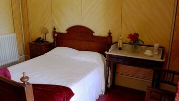 Una cama bien hecha con cabecera de madera, una mesita de noche con lámpara y un florero con una flor.