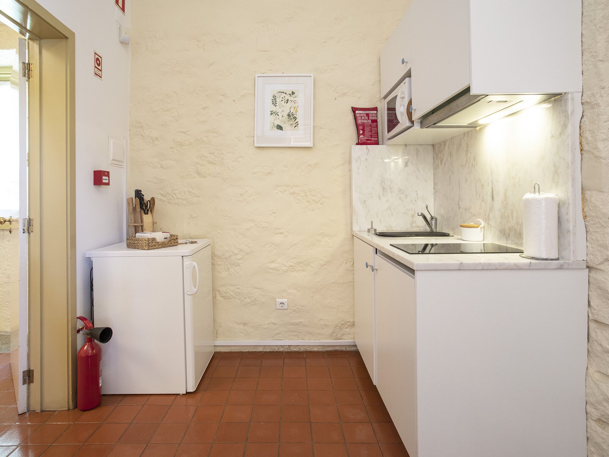 A compact kitchen with a white refrigerator, a small sink, and a tiled floor.