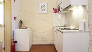A compact kitchen with a white refrigerator, a small sink, and a tiled floor.
