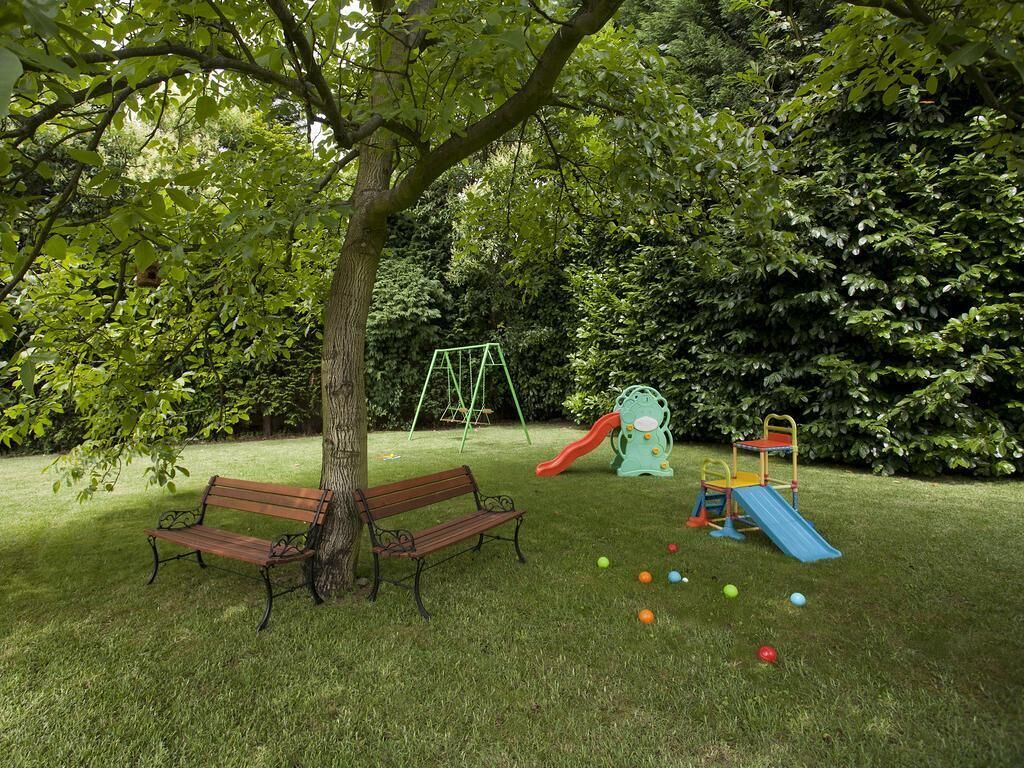 A park with a playground, two benches, and a tree.