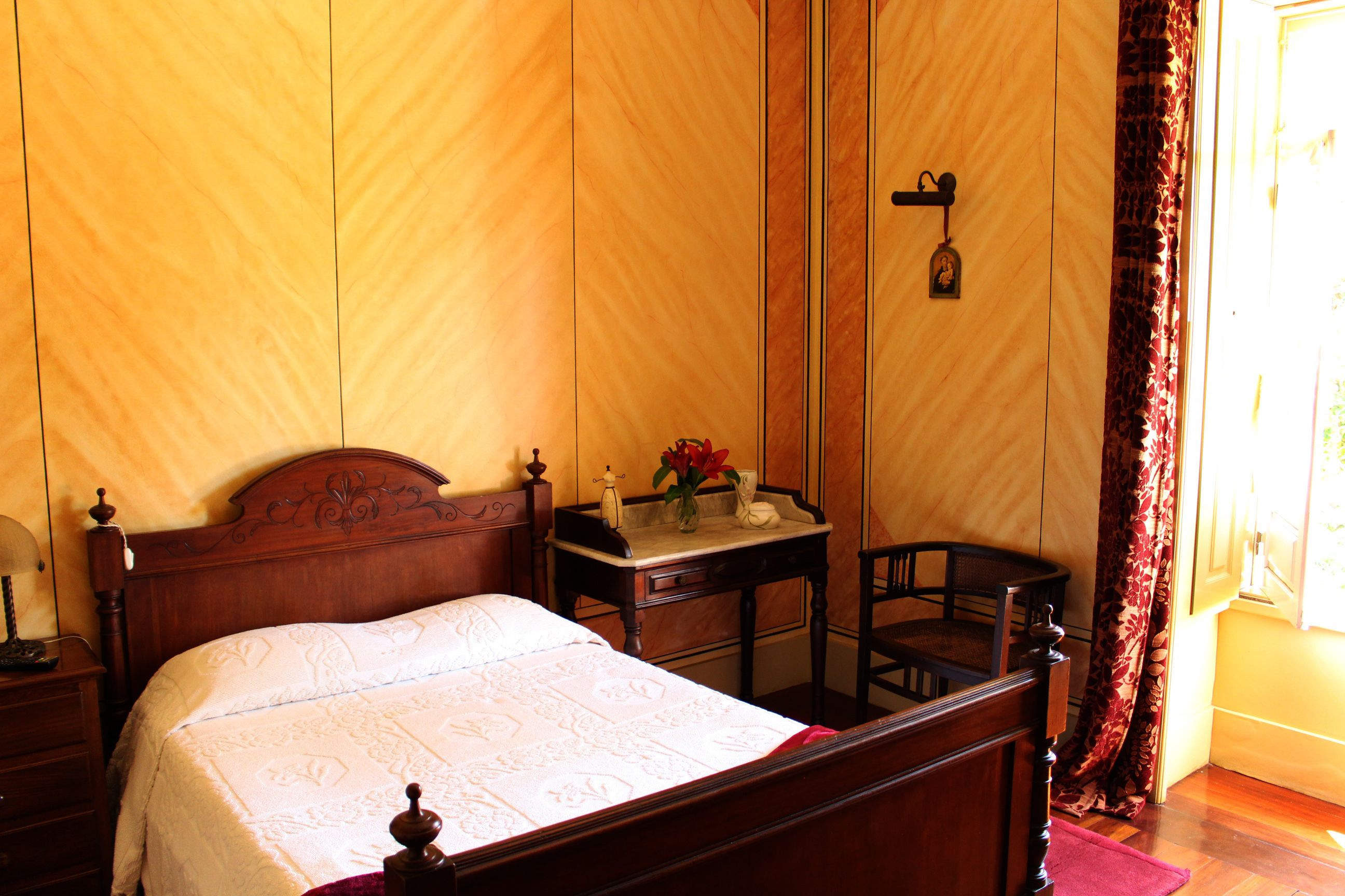 A wooden bed with a headboard, a bedside table with a lamp, and a chair.