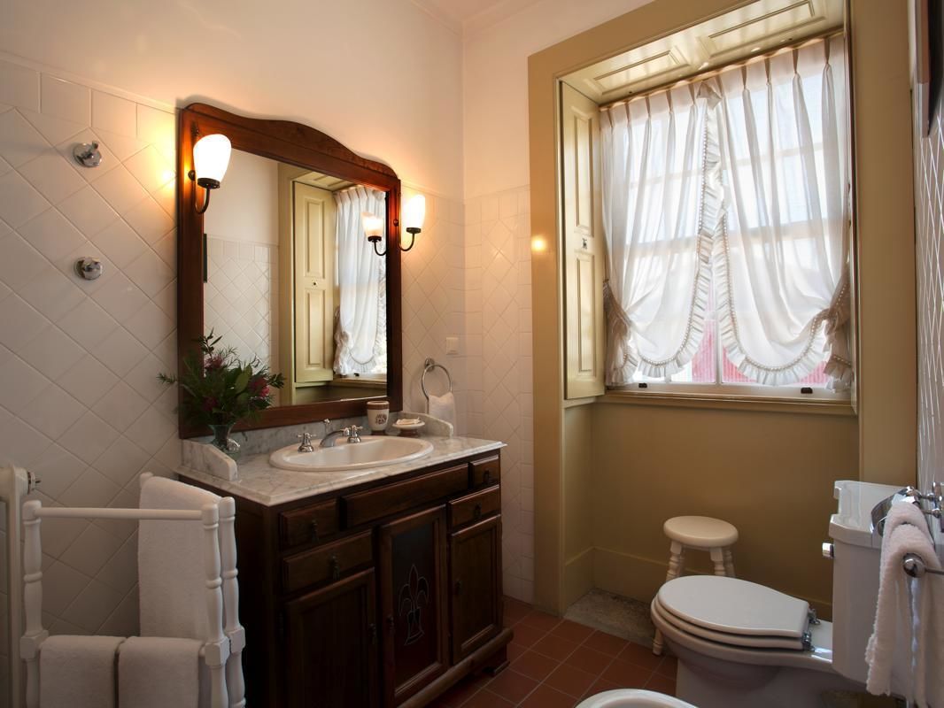 Uma casa de banho com um espelho grande, duas pias, uma sanita e uma janela com cortinas.