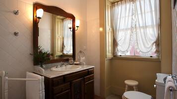 Uma casa de banho com um espelho grande, duas pias, uma sanita e uma janela com cortinas.