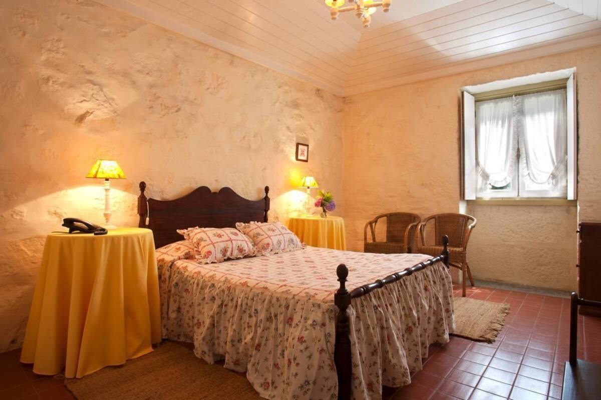 Une chambre à coucher avec un lit en bois, deux tables de chevet avec des lampes, une chaise et une fenêtre avec des rideaux.