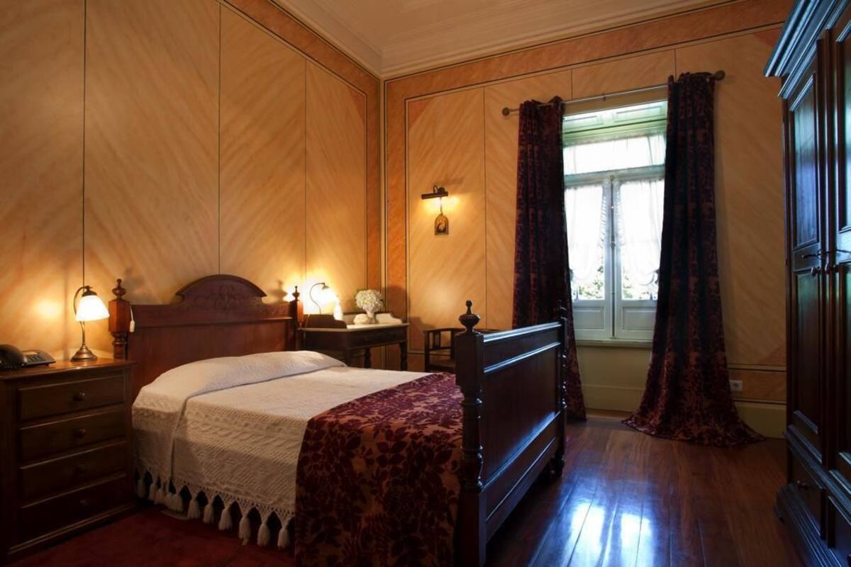 Une chambre à coucher avec une tête de lit en bois, une table de chevet avec une lampe, une commode et une fenêtre avec des rideaux.